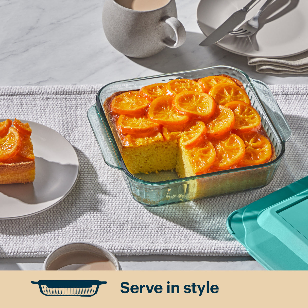 Glass dish with orange-topped dessert on a table setting with plates and cups.