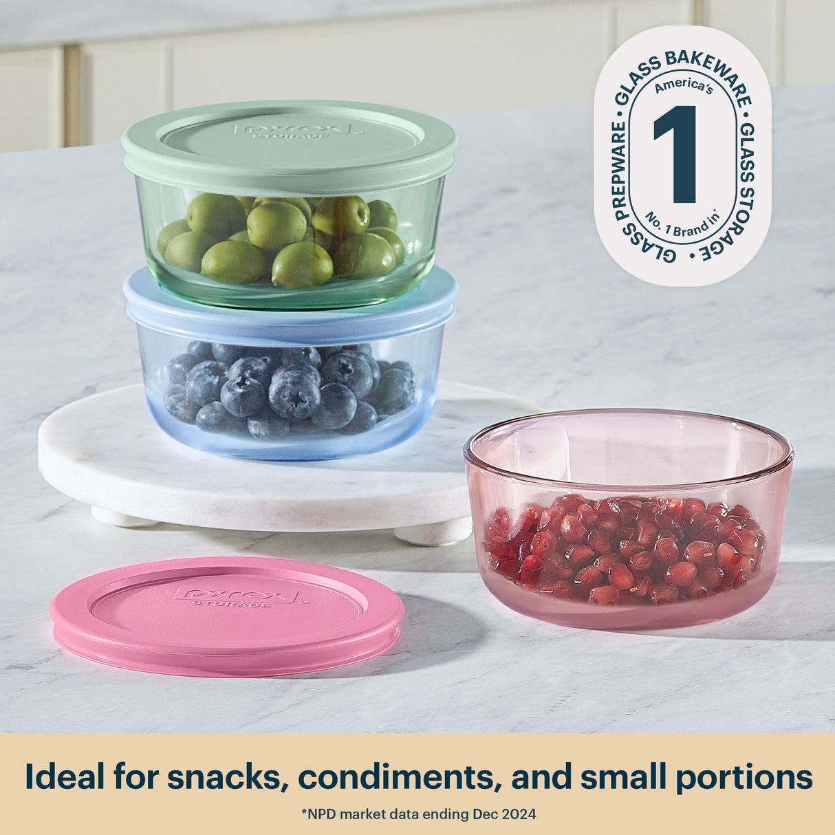 Set of glass food storage containers with lids on a marble surface, featuring the brand logo.