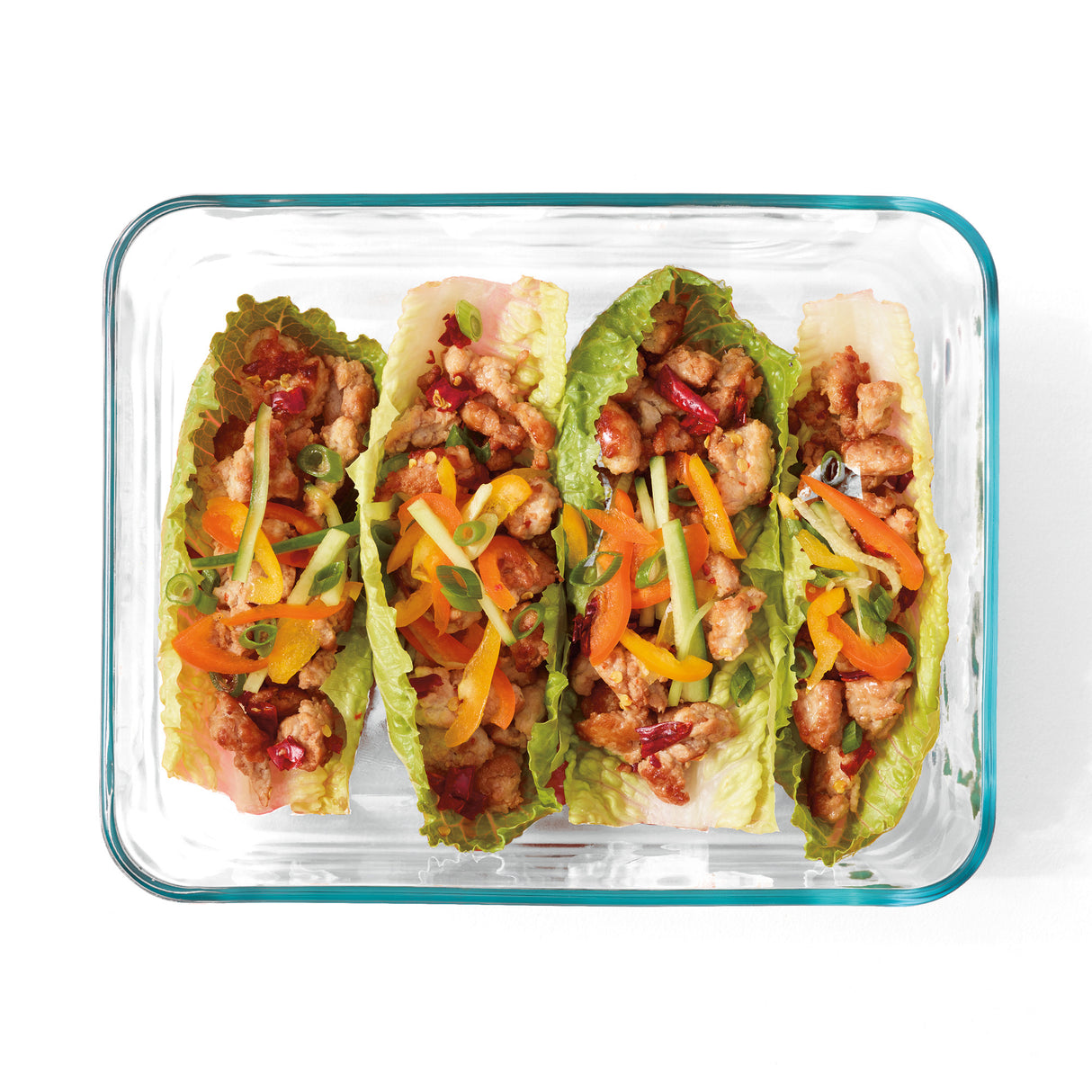 Glass container with lettuce wraps filled with meat and vegetables on a white background
