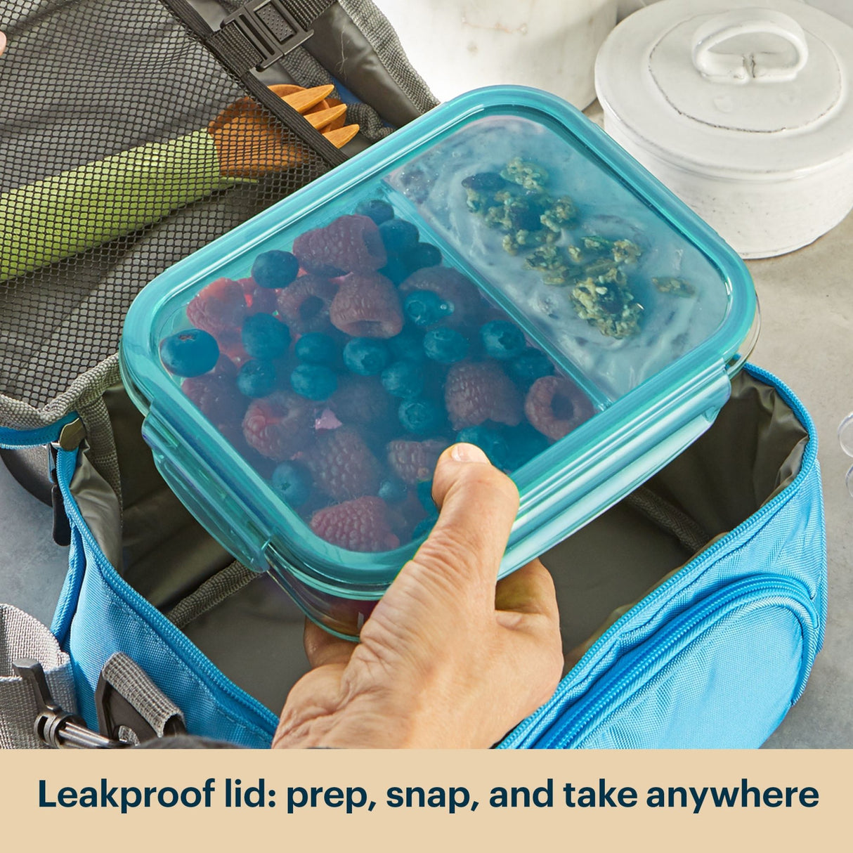 Hand holding a container with berries and greens, placed inside an insulated lunch bag with text 'Leakproof lid: prep, snap, and take anywhere'.
