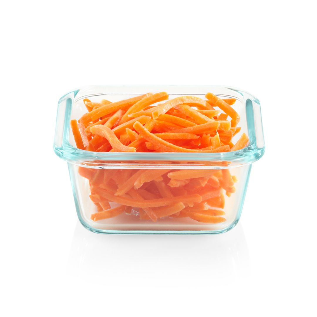 Glass container filled with orange shredded carrots on a white background