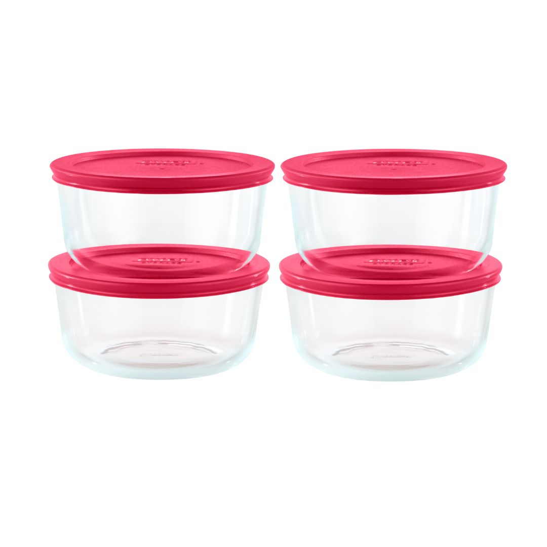 Set of four clear glass food storage containers with pink lids on a white background