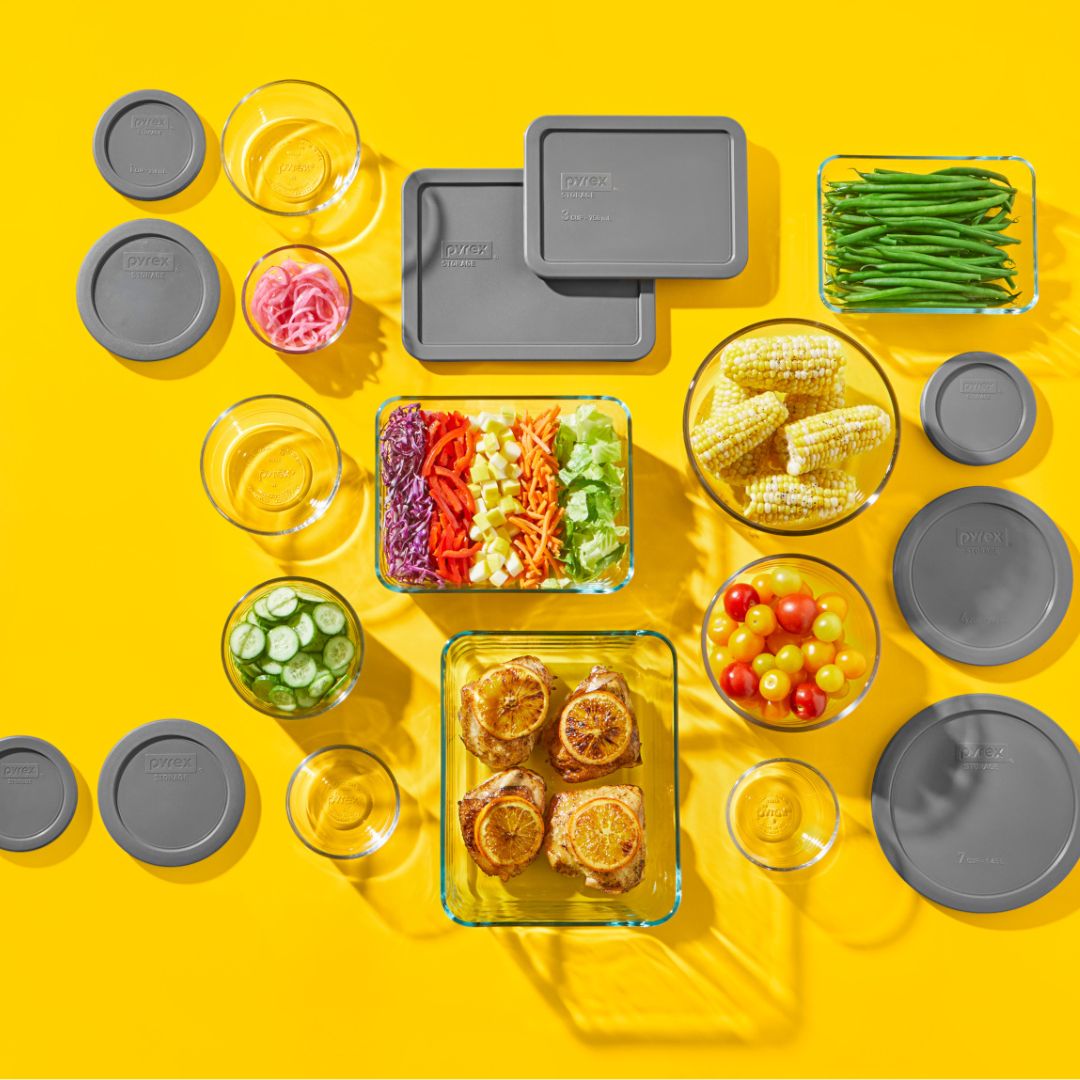 Pyrex glass storage set with gray lids and vibrant food on a yellow background