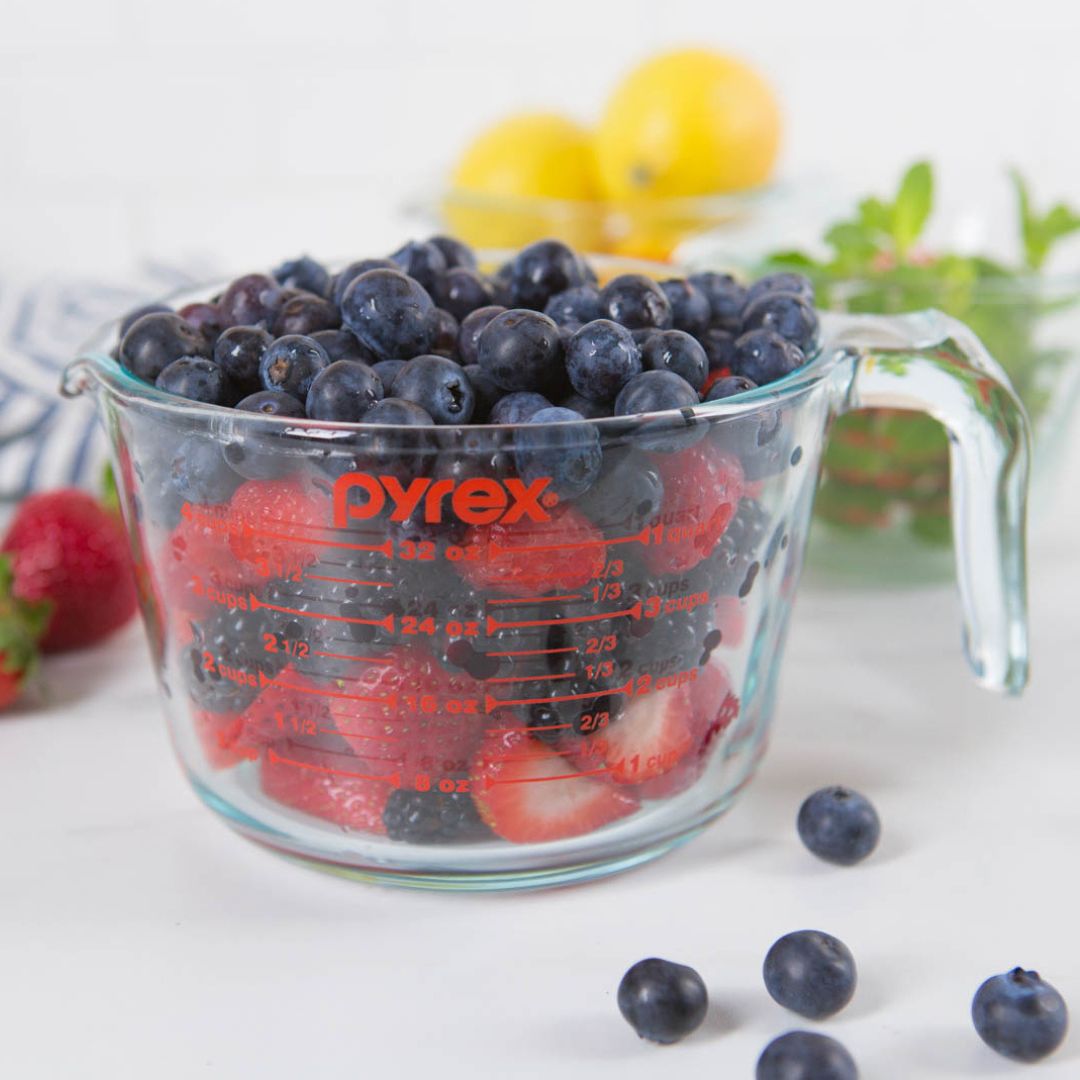 Pyrex measuring cup filled with blueberries and strawberries on a white surface