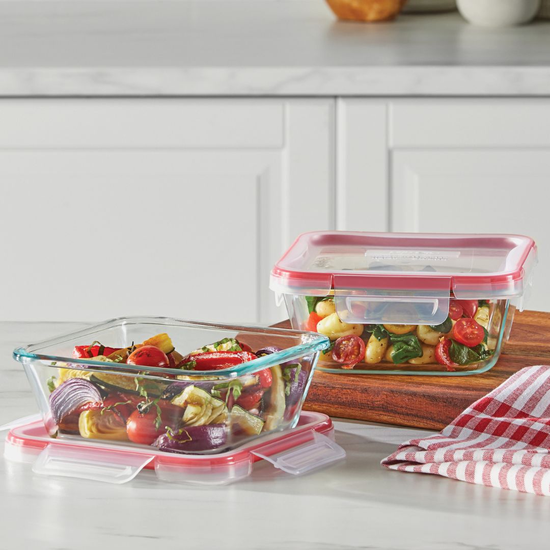 Glass food storage containers with red lids on a kitchen counter.