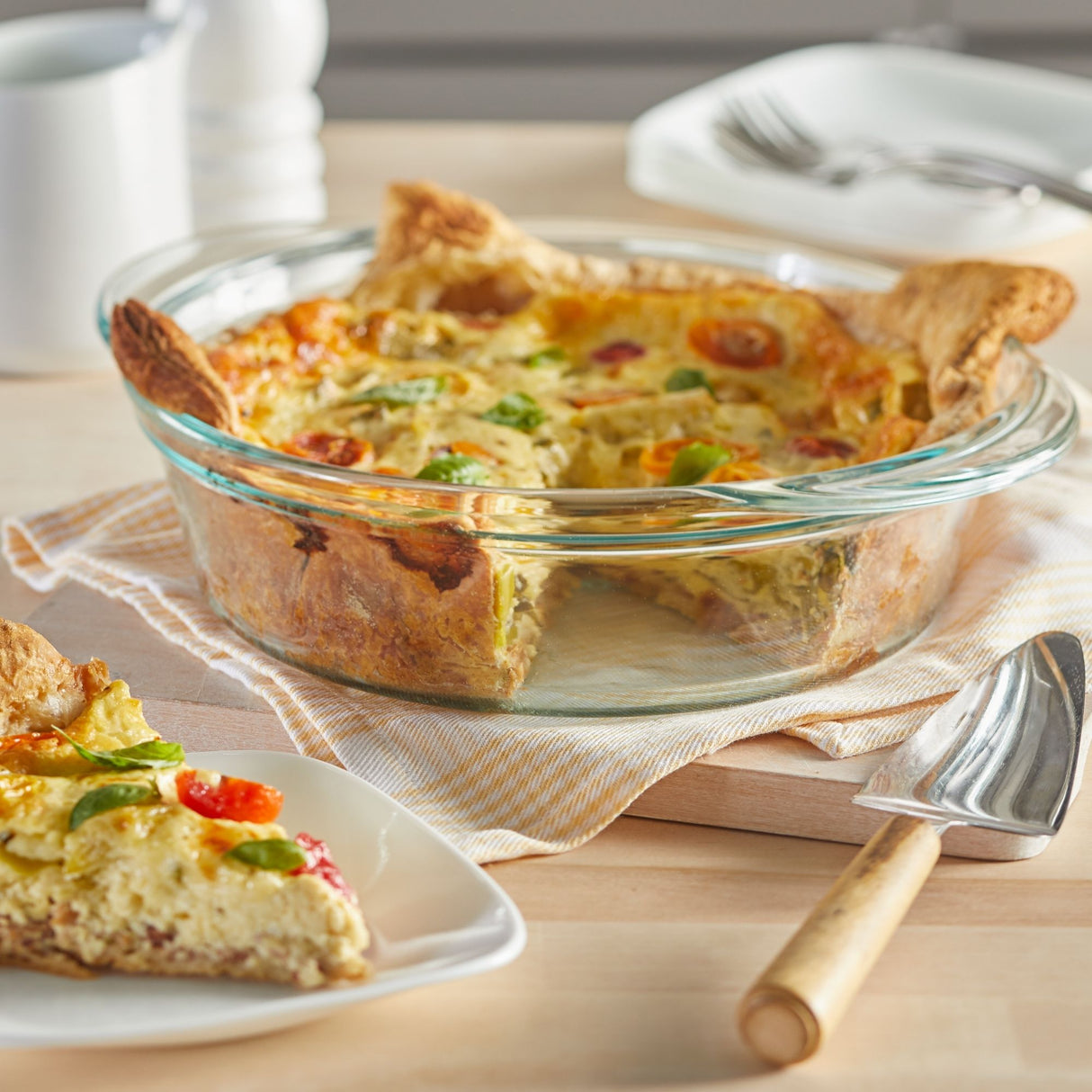 Savory baked quiche in a clear glass dish with a slice served on a plate.