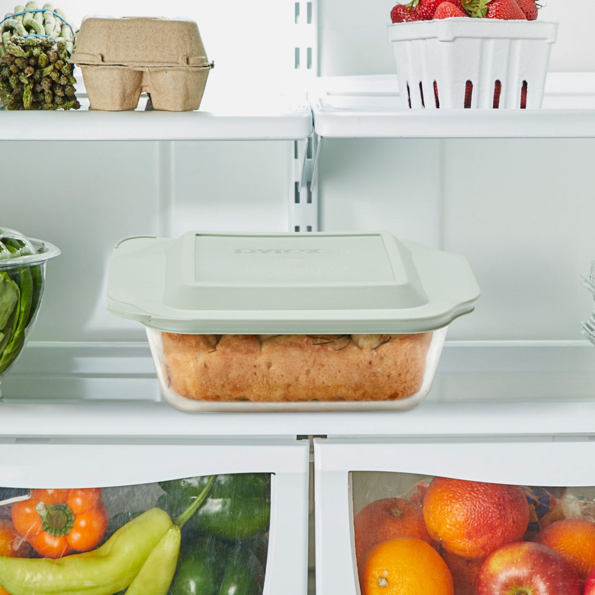 White refrigerator with a container of food on one of its shelves.